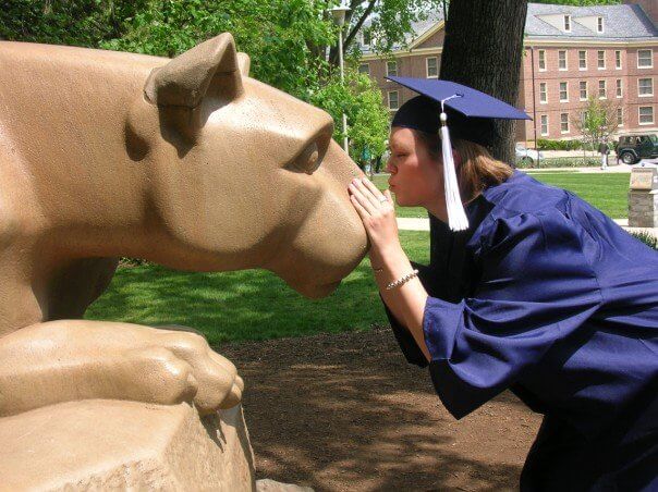 women in a graduation cap, kissing the penn state nittany lion statue.