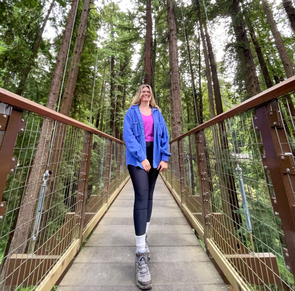 a woman standing on a sky bridge among tall trees