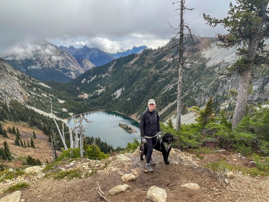 a women and a dog standing on the edge of a cliff overlooking a lake