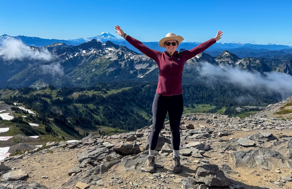 a woman standing with her arms open at the top of a mountain