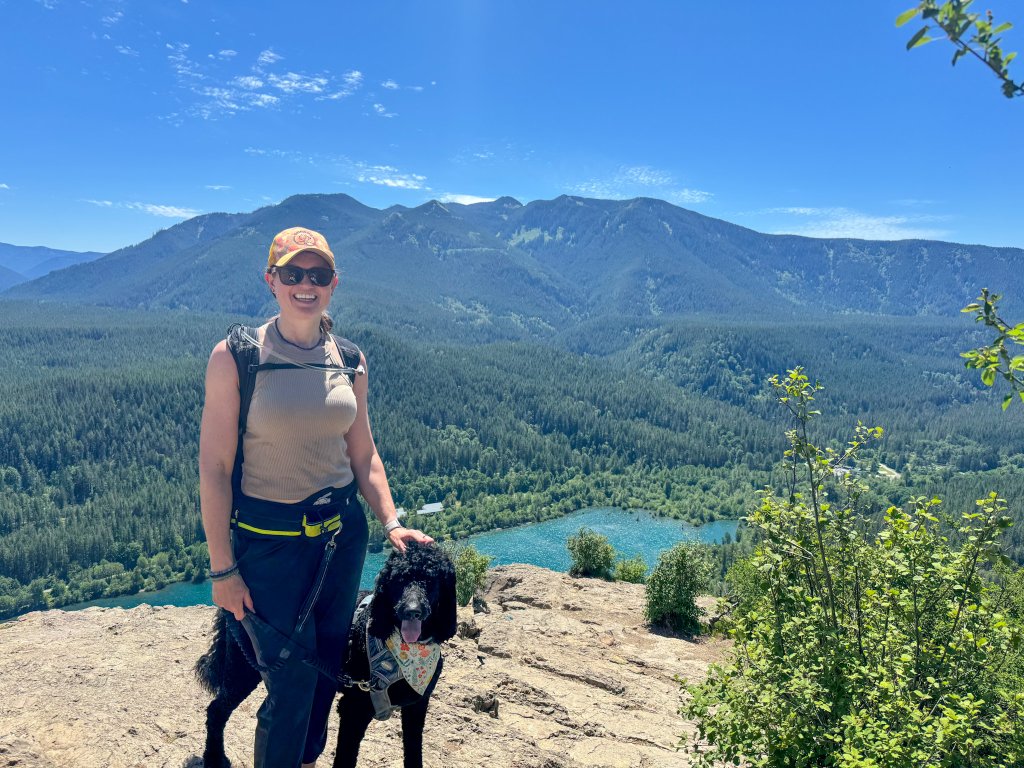 a woman and a dog on a mountain top by a lake

