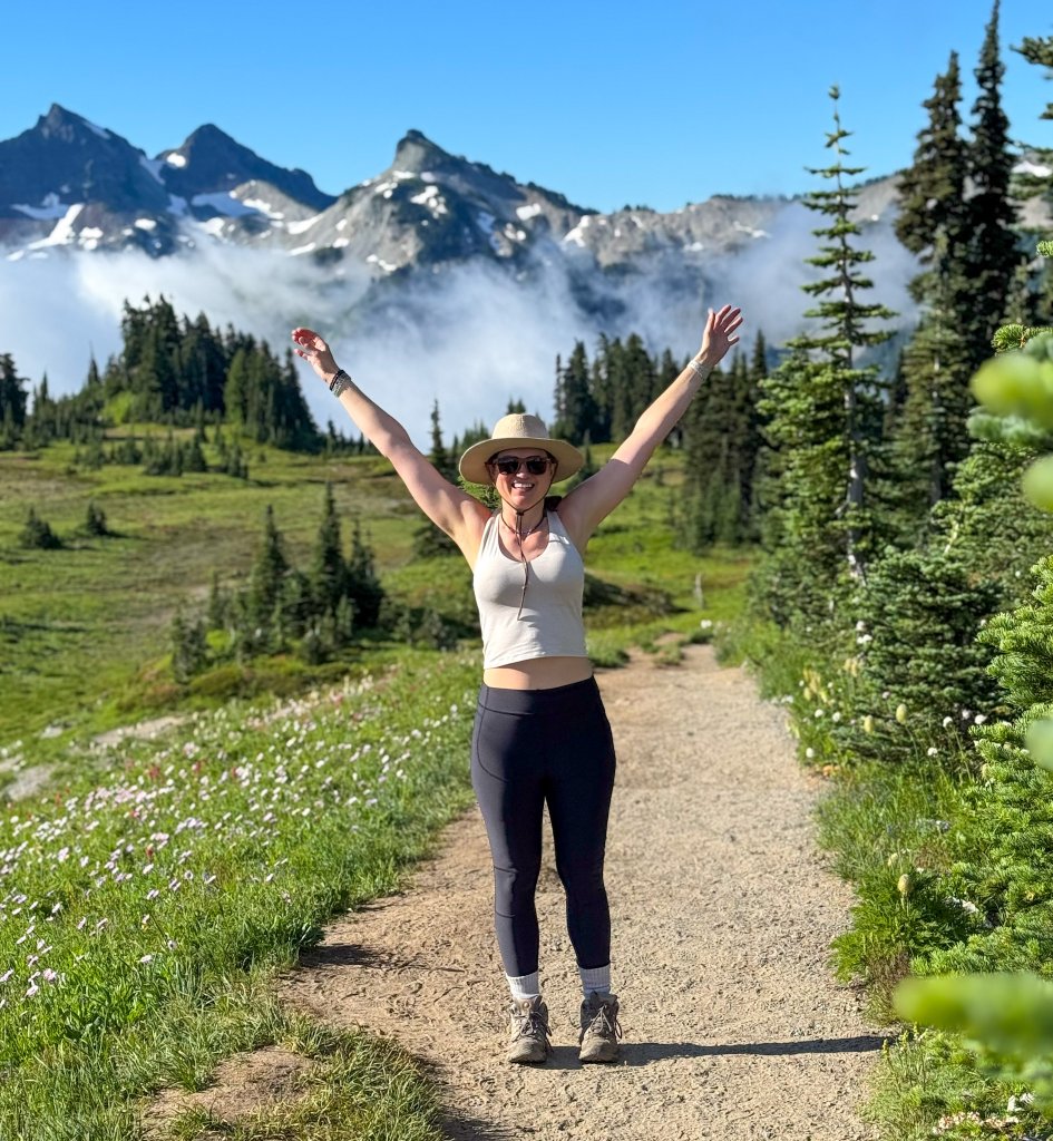 a women standing with her arms up by a mountain