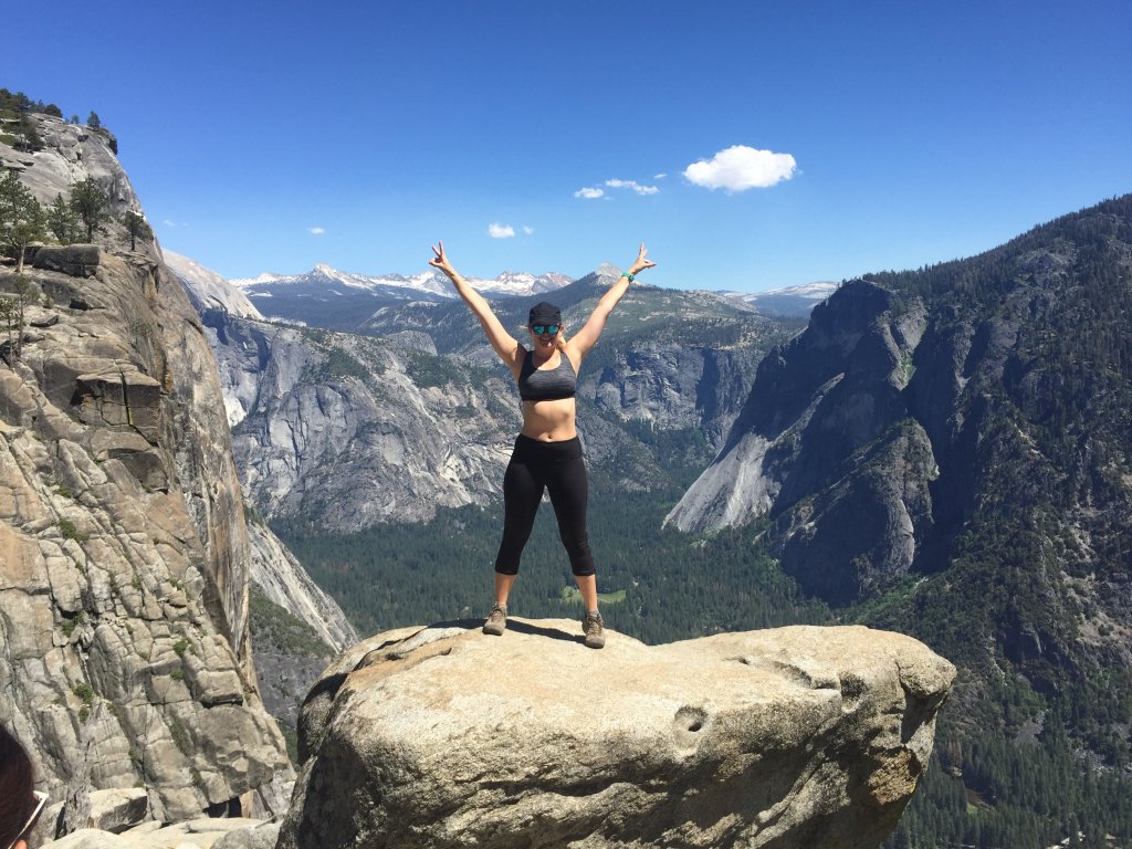 a woman standing on a peak at Yosemite with mountains in the background