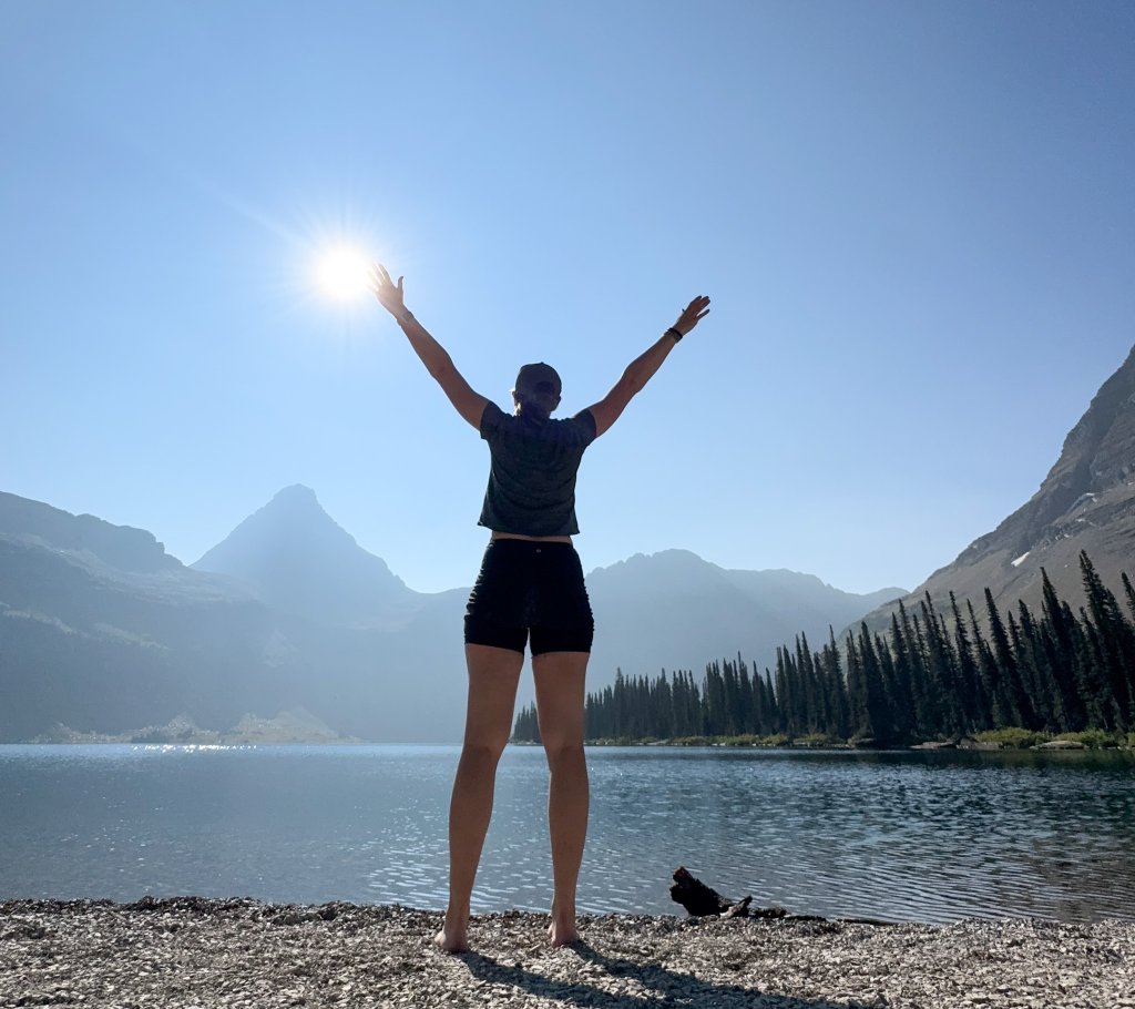 a woman with her arms in the air standing next to a lake