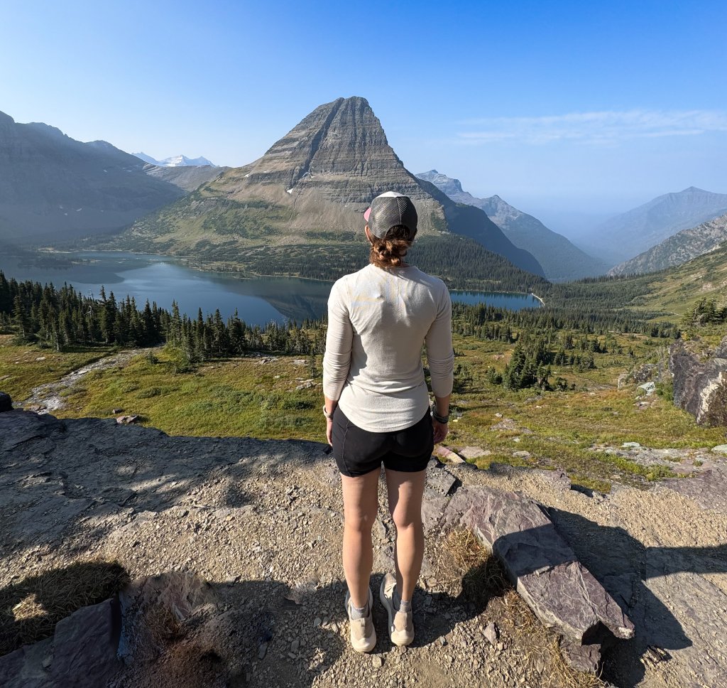 a woman standing at the edge of a cliff looking at a lake and mountain