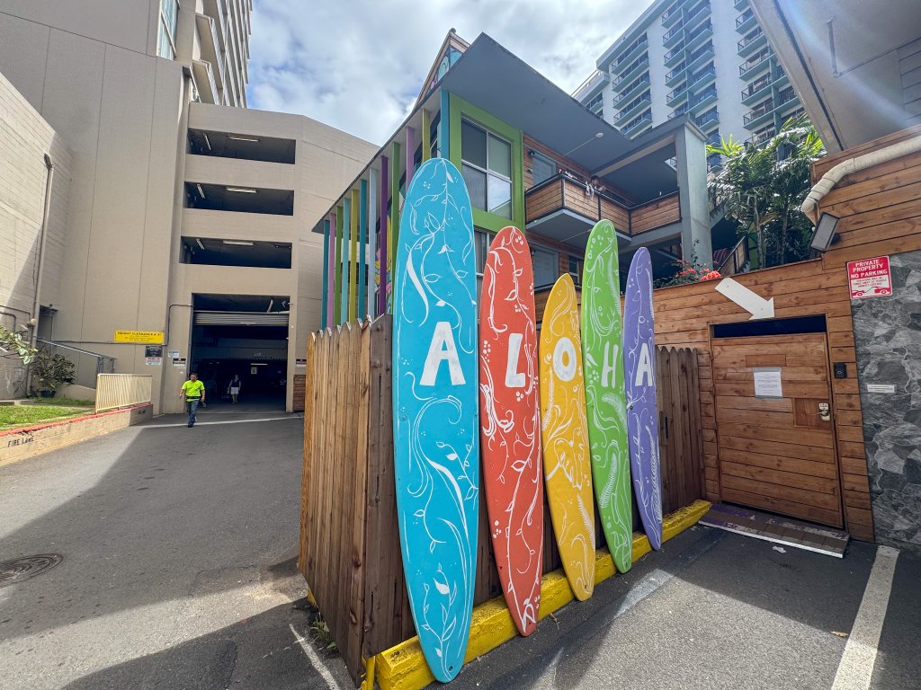 surf boards that say aloha in front of a hostel