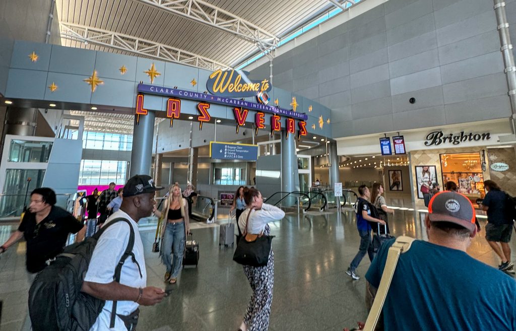 a sign that says "wecome to las vegas" and people walking around an airport